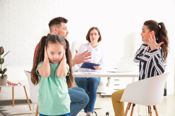 Sad child covering ears with hands because of her quarreling parents in psychologist's office