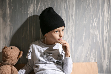Homeless little girl eating bread near grey wall