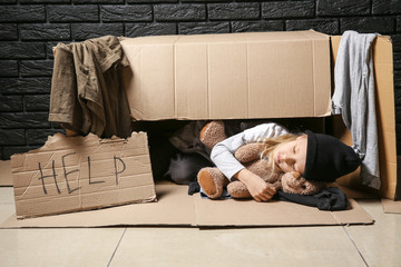 Homeless little girl with teddy bear sleeping in box