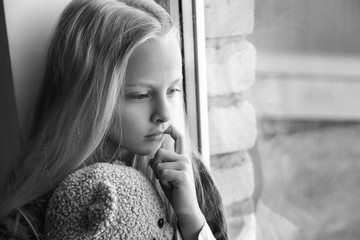Homeless little girl with teddy bear sitting on window sill