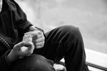 Homeless little boy with bread sitting on window sill indoors