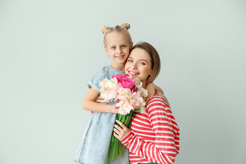 Little girl greeting her mother with bouquet of tulips on light background