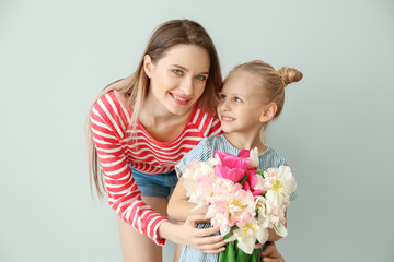 Little girl and her mother with bouquet of tulips on light background