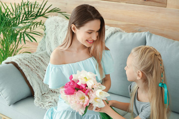 Little girl greeting her mother with bouquet of tulips at home