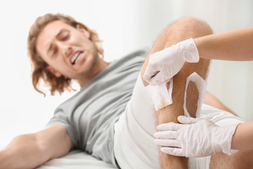 Fototapeta premium Man suffering from pain during wax epilation of legs in beauty salon