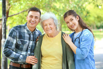 Caregiver and grandson walking with senior woman in park
