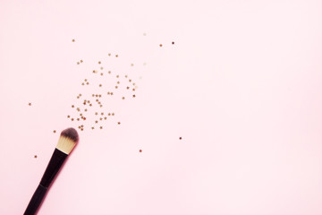 Pink makeup brush and spilling out gold star shaped confetti. Trendy pastel pink background. Makeup magic and festive vibes. Flat-lay, top view, copy space for your text.