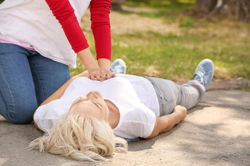 Female passer-by doing CPR on unconscious mature woman outdoors