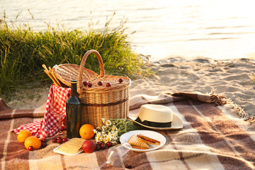 Wicker basket with tasty food and drink for romantic picnic near river - obrazy, fototapety, plakaty