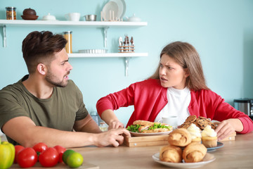 Young man trying to take tray with food from addicted woman in kitchen