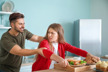 Young man trying to take tray with food from addicted woman in kitchen