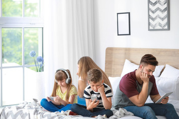 Family addicted to modern technologies with devices sitting on bed at home