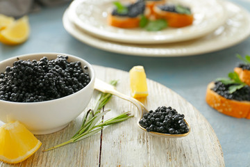 Bowl and spoon with black caviar on wooden board