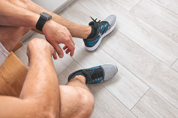 The young man is ready for morning running and sits on stairs in new sneakers