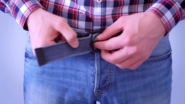 Man's hands unzip his jeans belt by hands, waist closeup. He is wearing plaid shirt and blue jeans.