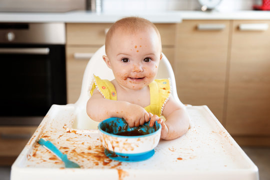 Cute baby in high chair making mess while eating puree