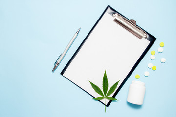 Top view of blank paper for writing doctor prescription. Marijuana leaf with medical pills on blue background. The concept of legalization of marijuana.