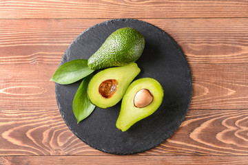 Slate plate with fresh ripe avocados on wooden background