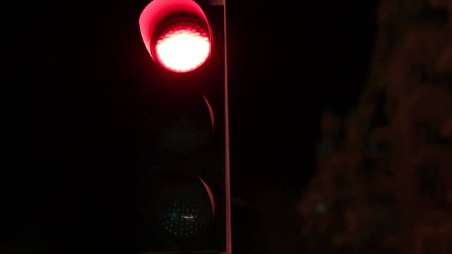 Stop light slowly changing from red to yellow to green light at night with buildings in the background.