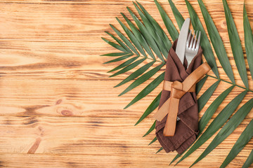 Cutlery, napkin and tropical leaf on wooden background