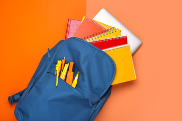 School backpack with stationery on color background