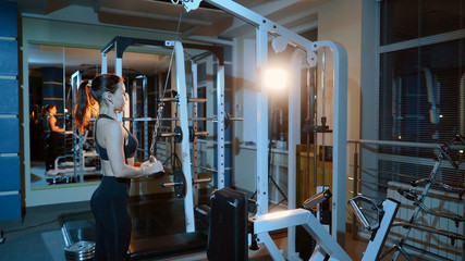 The girl performs the extension of the arms for the triceps in a block simulator.