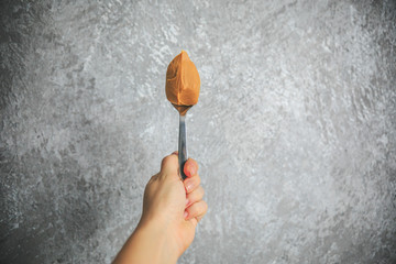 Peanut butter on the spoon holding in hand on the gray and white background.