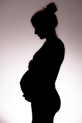 Silhouette einer schwangeren jungen Frau, H&auml;nde oberhalb und unterhalb des Bauches, Blick nach unten