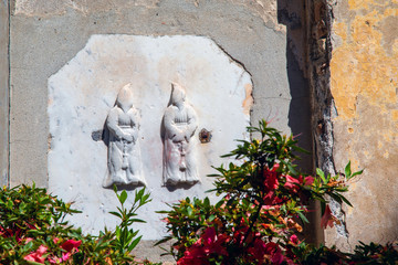 Rapallo, Genoa / Italy - April 28 2019: Close-up of a bas-relief in white marble (XIV-XV century) representing two members of the confraternity of Disciplinati on the façade of Oratory of Bianchi