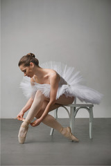 ballerina in a white dress sitting on a chair and tying her ballet slippers, for wall background. © pavlobaliukh