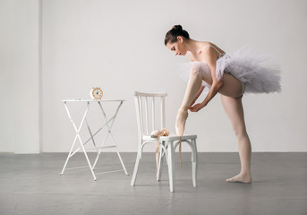 ballet dancer in a white dress with chair tying her ballet slippers, for wall background. © pavlobaliukh