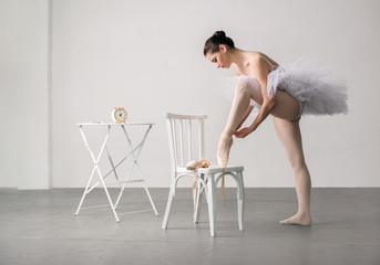 ballet dancer in a white dress with chair tying her ballet slippers, for wall background.