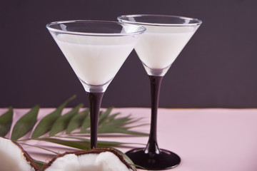 Pina Colada cocktail on the pink table with palm leaf and coconut on the blue table