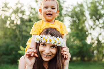 Mother giving piggyback ride to her loving daughter outside in nature. Hippie mother and happy baby...