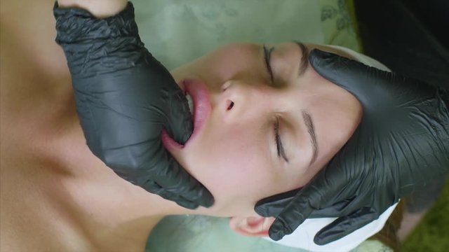 Manual sculpting face massage for young woman in beauty clinic. Massage therapist in gloves is working on woman's jaw inside her mouth making facial buccal massage, top view.
