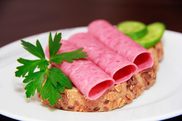 sandwich of rye bread with meat sausage, cucumbers and parsley