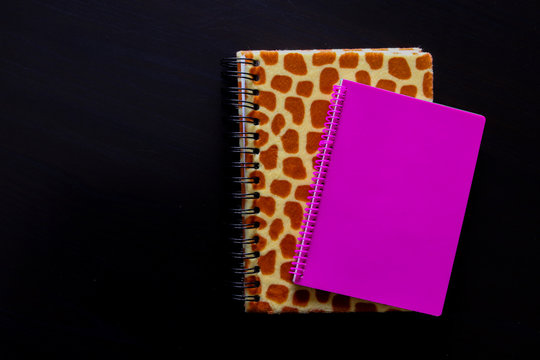 Dettaglio di un quaderno leopardato e quaderno rosa con lo sfondo nero vista dall&rsquo;alto, oggetti da ufficio