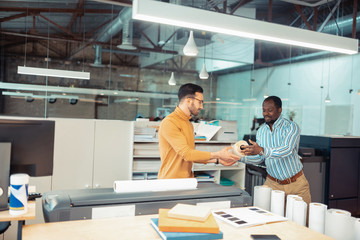 Dark-skinned colleague giving roll of paper to writer