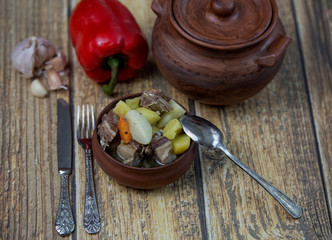 Roast cooked in a clay pot, red pepper, garlic on a wooden background