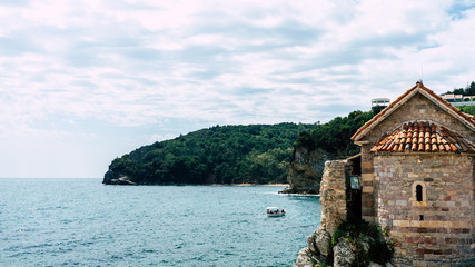 Tower of old fortress, embankment and sea bay in the town of Budva, Montenegro. Round tower with red tiled roof at the wall of the old town. Green cliff in Adriatic sea