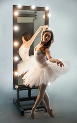 Fototapeta premium Young beautiful ballerina is posing near big mirror with gray floor