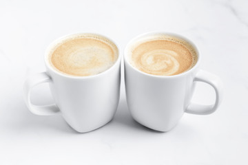 Minimal desk top with two white cups of coffee on marble table. Close-up. Space for text .