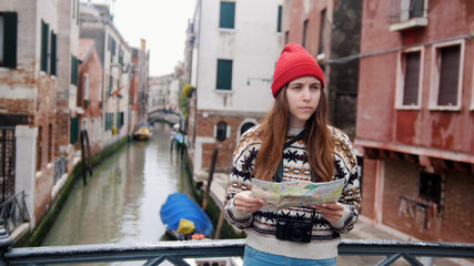 A young confused woman standing above the water channel and looking at the map - Venice, Italy