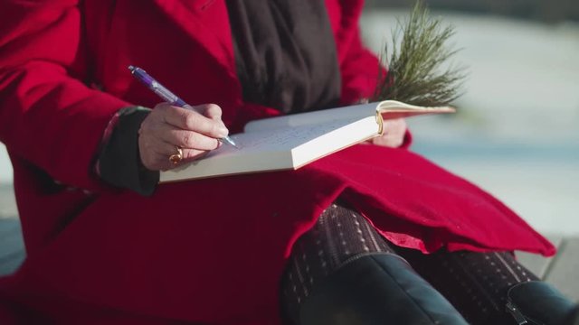 Woman in Red Coat Sitting outside while Writing in a Book