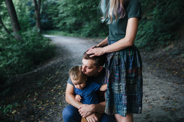 Happy young family father, mother and little son hugging and touching outdoors, playing together in summer park