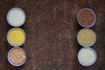 Raw cereals in bowls on the decorative background. Ingredients for cooking baby porridge or side dish. Buckwheat, peas, semolina, wheat, rice, corn grits on the burlap texture. Diet food