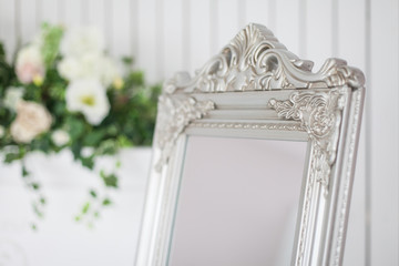Mirror in classic bright interior with fireplace and armchair. Spring interior decoration with flowers.