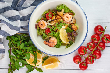 seafood salad decorated with cherry tomatoes mint and lemon at white wooden table top. Salad with prawns, mussels andsquid.