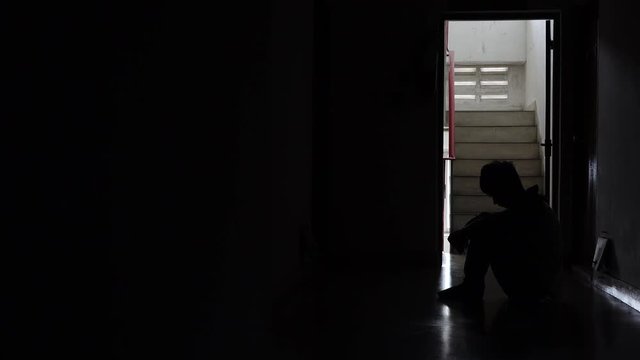 Silhouette of a sad young man sitting in the dark leaning against the wall in old condo, Domestic violence, family problems, Stress, violence, The concept of depression and suicide.