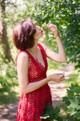Young brunette woman in red dress eats red currant in the forest